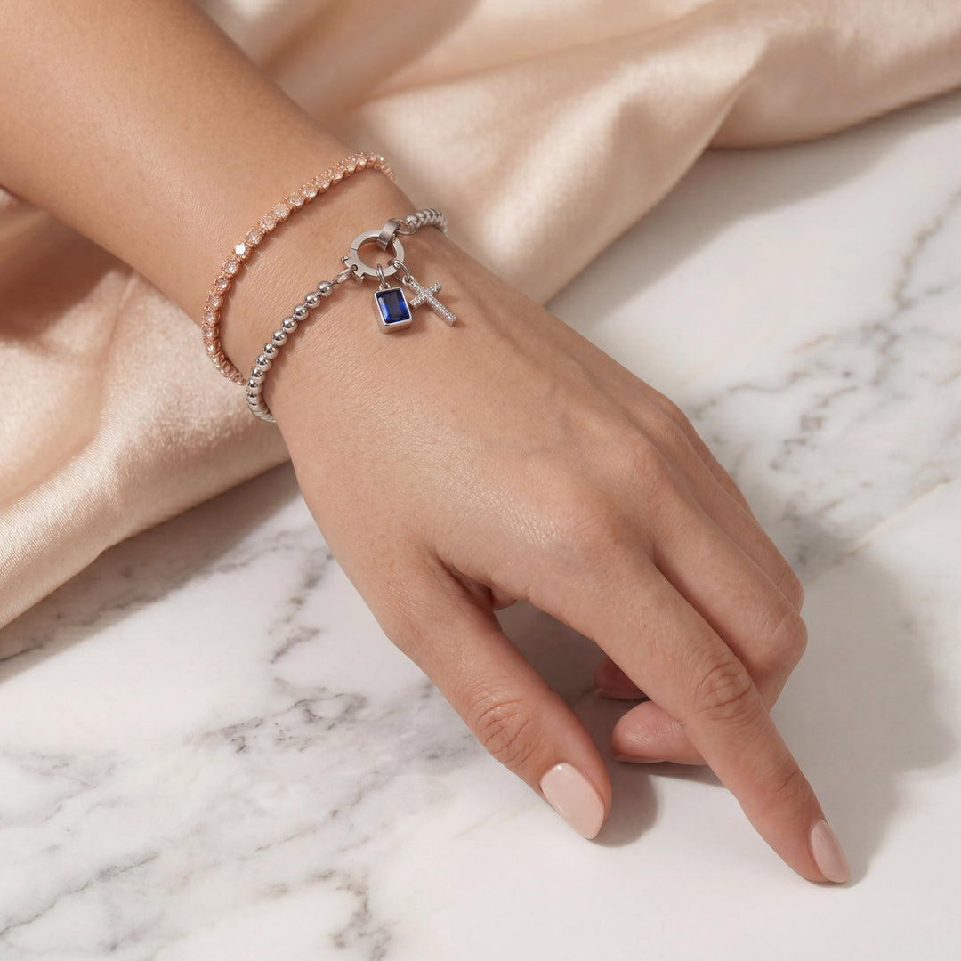 Pulsera de Auxana con dije de cruz y piedra natal, joyería elegante en plata con detalles religiosos y piedras brillantes.