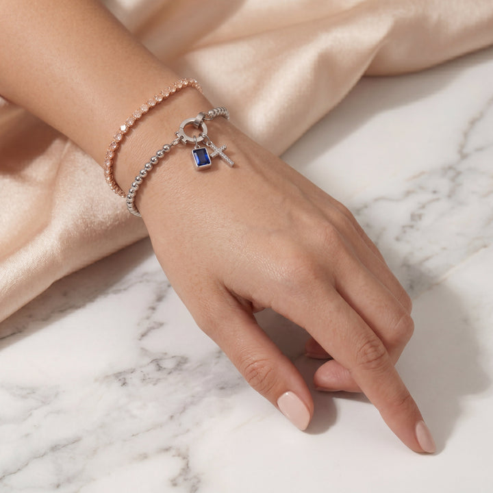 Pulsera de Auxana con dije de cruz y piedra natal, joyería elegante en plata con detalles religiosos y piedras brillantes.