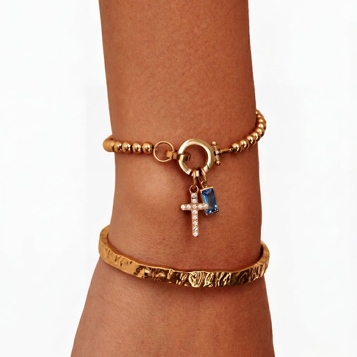 Pulsera de Auxana con dije de cruz y piedra natal, diseñada en plata con detalles elegantes y simbólicos.