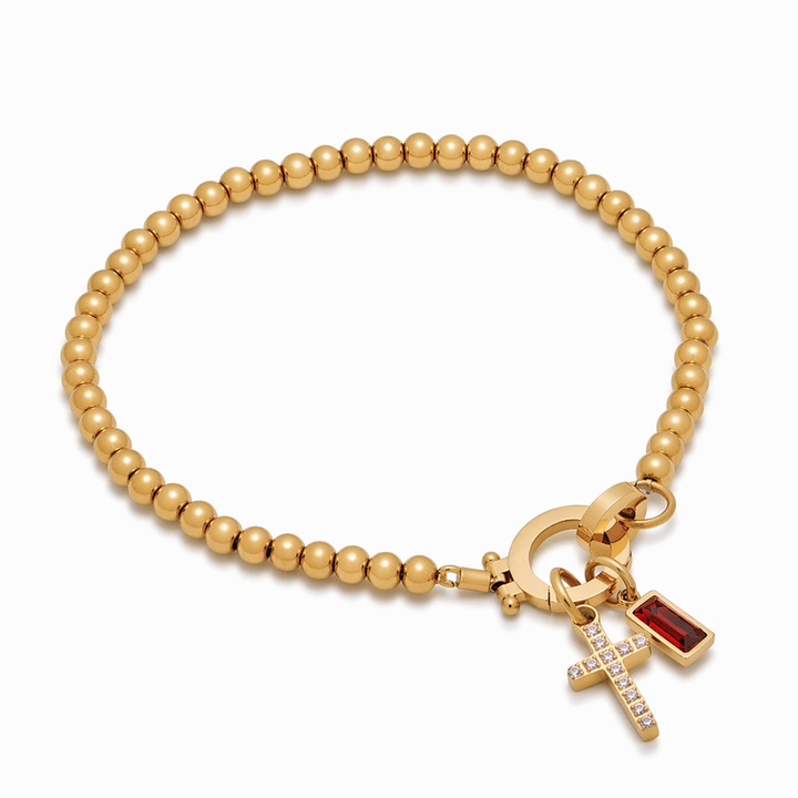 Pulsera de Auxana con dije de cruz y piedra natal, accesorio de joyería con detalles delicados y significado simbólico.
