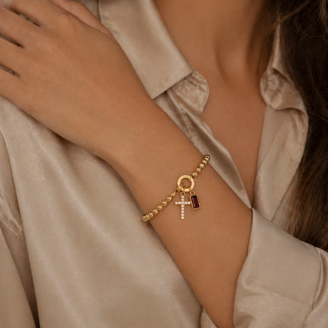 Pulsera Auxana con dije de cruz y piedra natal, joyería en plata con detalles religiosos y piedra semipreciosa.